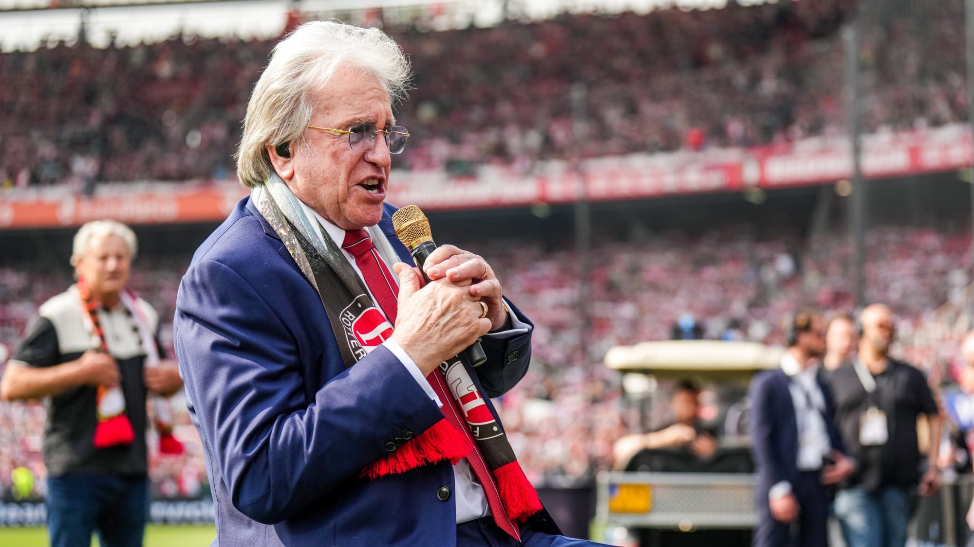 Lee Towers singing with a microphone and Feyenoord scarf in a packed De Kuip.