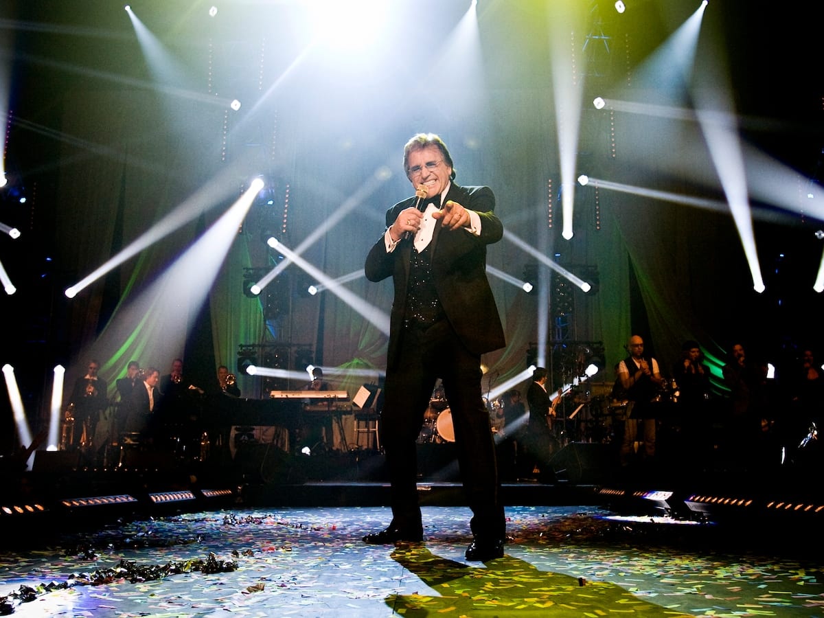 Lee Towers singing on stage at a gala concert under the spotlights.